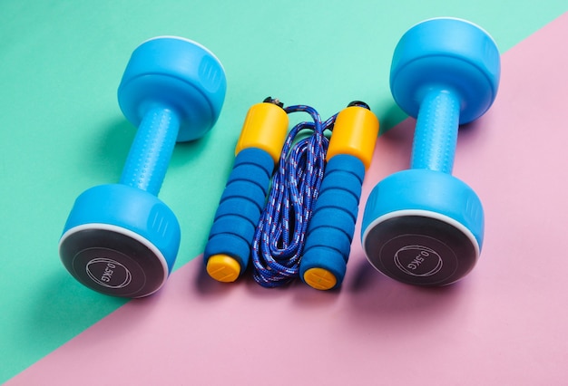 Photo colored jumping rope, dumbbells on a pink-blue pastel background. minimalism sport concept.