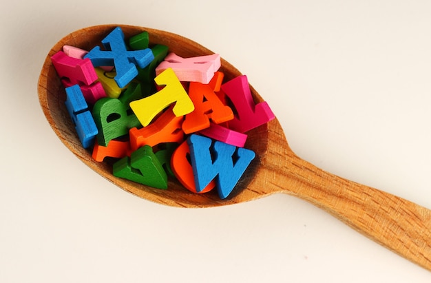 Colored letters in a spoon on a white surface as a symbol of knowledge and learning