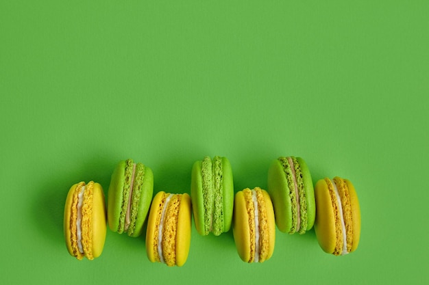 Colored macaron or macaroon sweet meringuebased confection on green background Closeup copy space