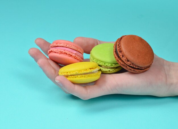 Colored macaroons in hand close-up on a blue surface