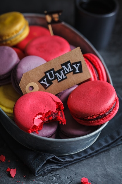 Покрашенные macaroons в металлическом блюде, темной предпосылке.