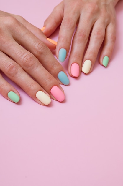 Manicure colorata opaca sulle mani femminili su una superficie rosa