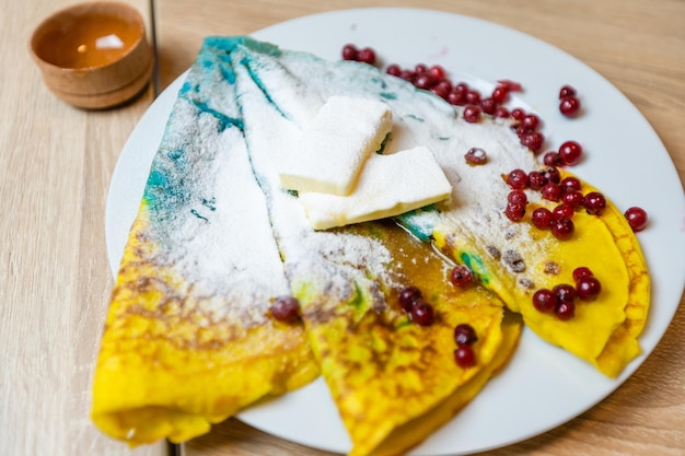 Colored pancakes with berries, butter and honey