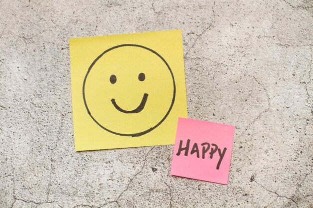 Photo colored paper notes with happy drawing face and single word on a gray marble background