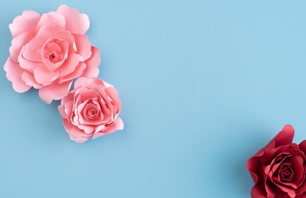 Colored paper roses on blue background Copy space