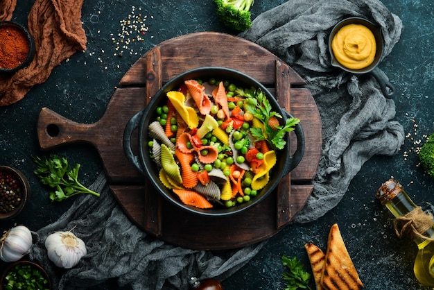 Colored pasta with peas and vegetables in a black bowl Top view Free space for text