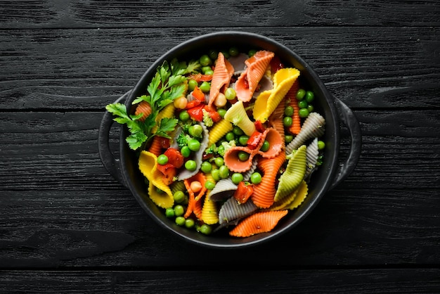 Colored pasta with peas and vegetables in a black bowl Top view Free space for text