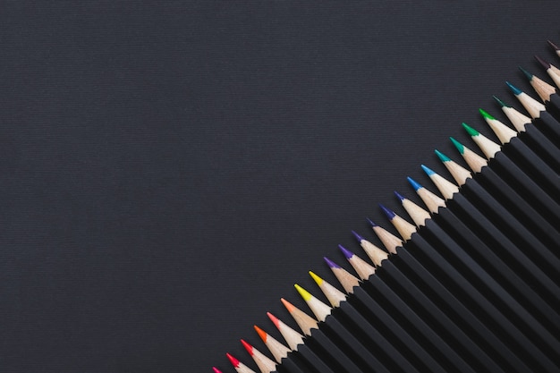 Colored pencil set arranged in diagonal on black background. Stationery backdrop for your design, copy space.