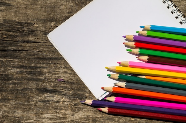 Colored pencils and blank notepad on old wooden desk