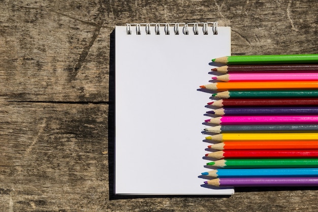 Colored pencils and blank notepad on old wooden desk