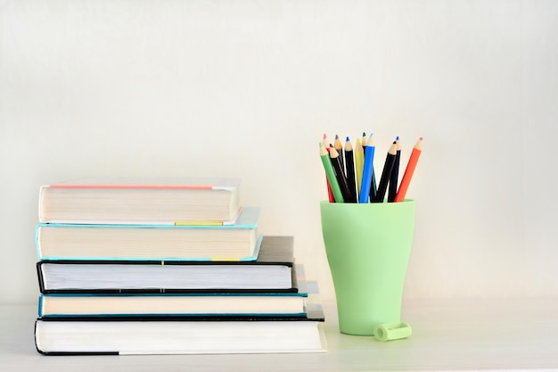 Colored pencils in a holder and a stack of books on a white table Back to school