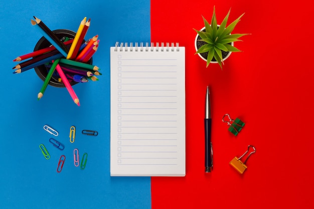 Colored pencils,notebook, colored paper clips, pen, flower on a red-blue background. 