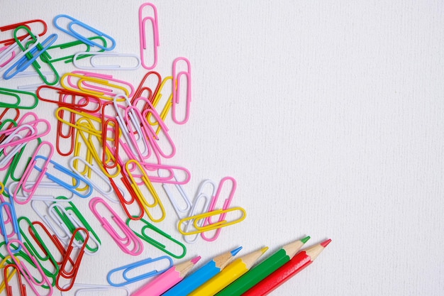 Цветные карандаши и скрепки на белом фоне школьные принадлежности и канцелярские принадлежности