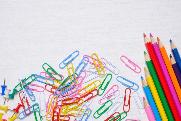 Цветные карандаши и скрепки на белом фоне школьные принадлежности и канцелярские принадлежности