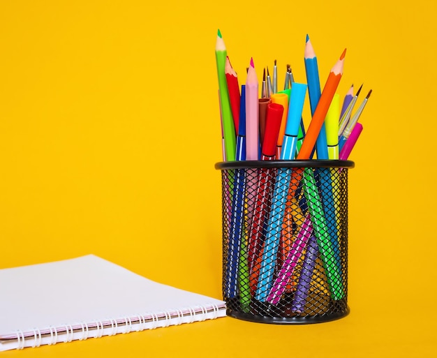 Colored pencils in a pencil case on a yellow background with a white sheet of paper