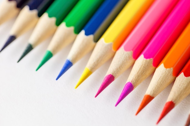 Colored pencils rainbow laid out side by side one to other on white background rod writing material closeup selective focus