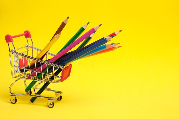 Colored pencils in shopping cart on yellow background.School supplies for drawing.