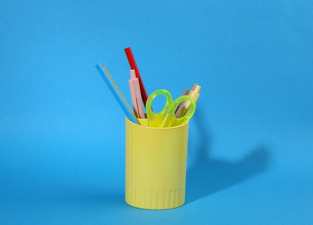 Photo colored pencils and various colorful stationery for school in holder or cup on blue background