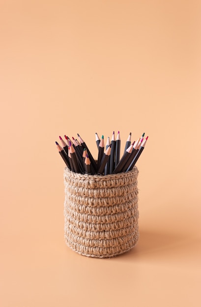 Colored pencils in a wicker basket made of jute on beige