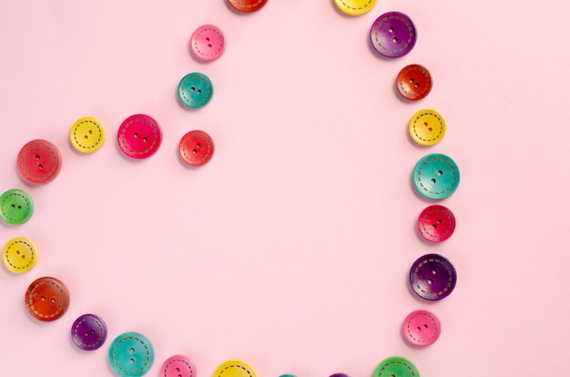 Colored sewing buttons composition on pink background.