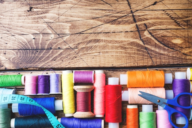 Colored spools of thread laid out in rows on wooden background. Copy space.