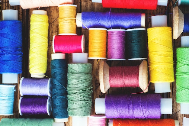 Colored spools of thread laid out in rows on wooden background.