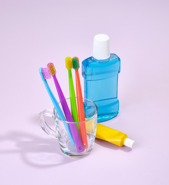 Colored toothbrushes stand in a glass cup on the table Blue mouthwash and a tube of toothpaste