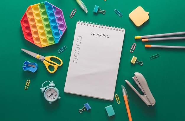 Colored various school supplies and an alarm clock on a green paper background back to school and ed...