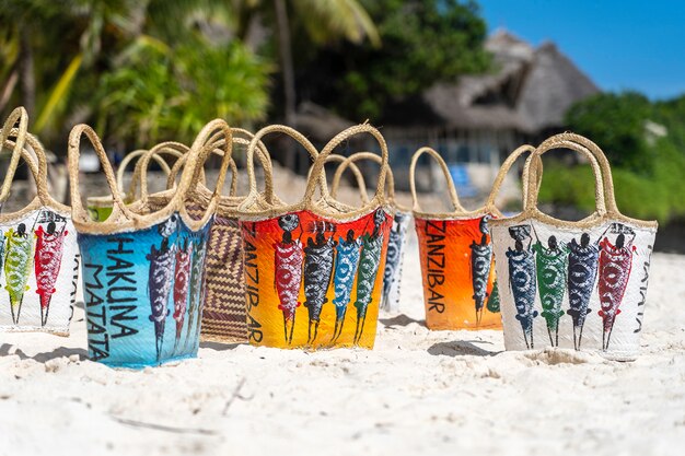 Colored wicker woman bags in typical zanzibar style on the white sandy beach near turquoise ocean of Zanzibar island