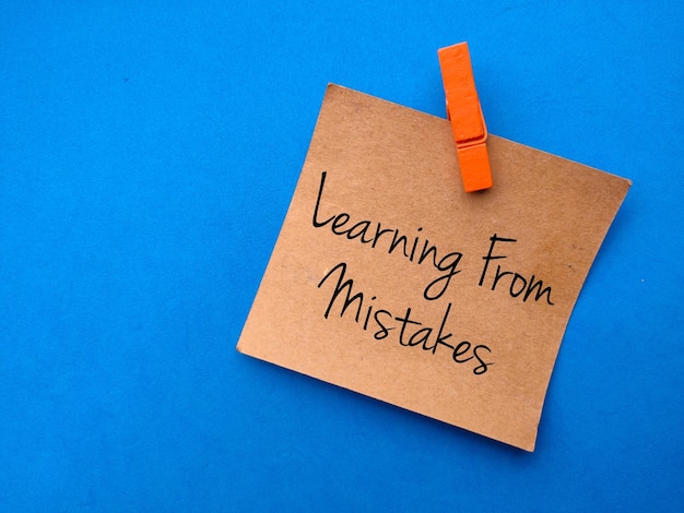 Цветные деревянные скрепки с коричневой карточкой, написанные текстом Learning From Mistakes на синем фоне