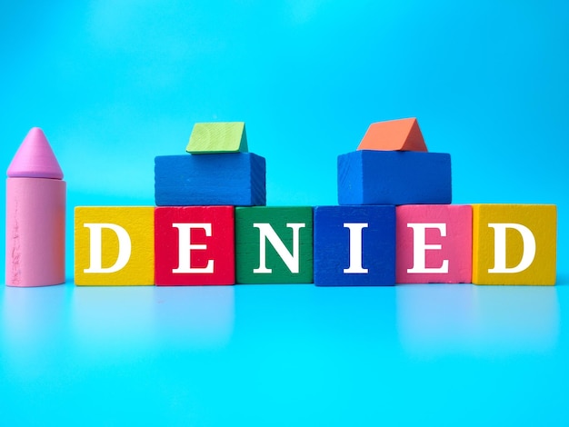 Photo colored wooden cube with word denied on a blue background