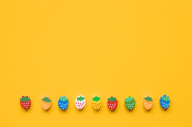 Colored wooden figures in the form of strawberries on a yellow background