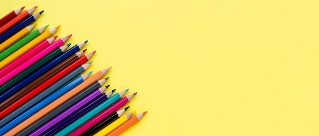 Colored wooden pencils row on yellow background closeup Copy space