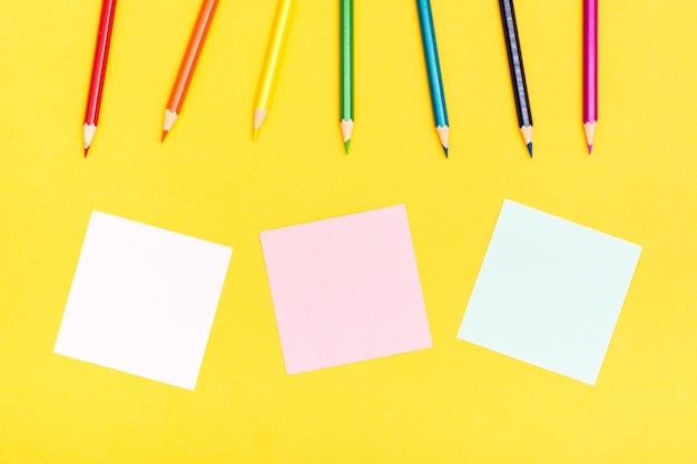 Colored wooden pencils and sheets for writing on a yellow background