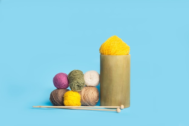 Colored wool balls and knitting needles on a light blue background with copy space