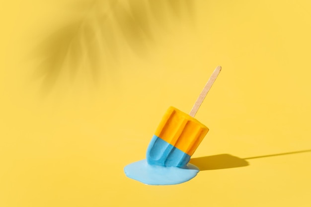 Colored yellow and blue ice cream melts from the hot sun Palm leaves shadow Hot weather concept