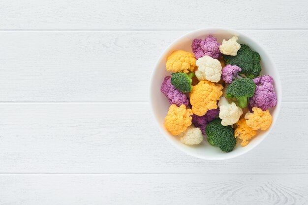 Colorfu cauliflower Cauliflower cut into small pieces white bowl on light stone marble concrete background Purple yellow white and green color cabbages Agricultural harvest Mock up Top view