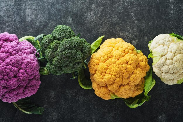 Colorfu cauliflower Various sort of cauliflower on old dark gray concrete background Purple yellow white and green color cabbages Broccoli and Romanesco Agricultural harvest Mock up