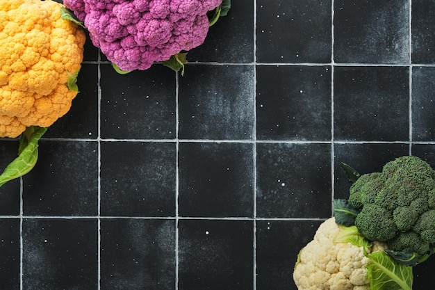 Colorfu cauliflower Various sort of cauliflower on old stone tiles black concrete background Purple yellow white and green color cabbages Broccoli and Romanesco Agricultural harvest Mock up