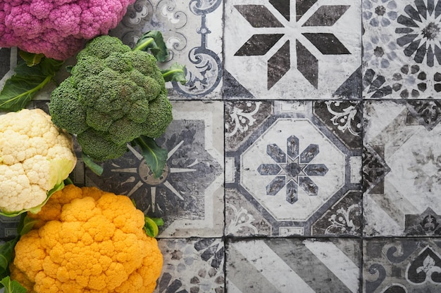 Colorfu cauliflower various sort of cauliflower on stone tiles\
gray concrete background purple yellow white and green color\
cabbages broccoli and romanesco agricultural harvest mock up