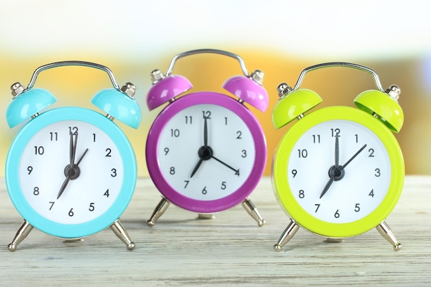 Colorful alarm clocks on table on bright background