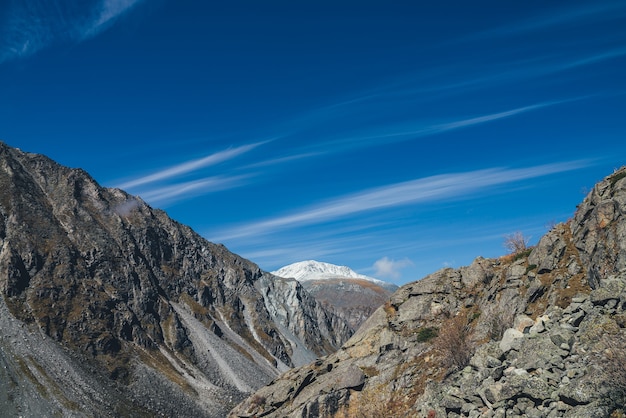 Красочный альпийский пейзаж с большой горой в осенних цветах со снегом на пике под перистыми облаками в голубом небе. Потрясающие осенние пейзажи со скалами и заснеженной вершиной горы. Живописный вид на горы.