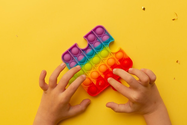 Красочные антистрессовые сенсорные игрушки fidget push popit в руках ребенка на желтом фоне
