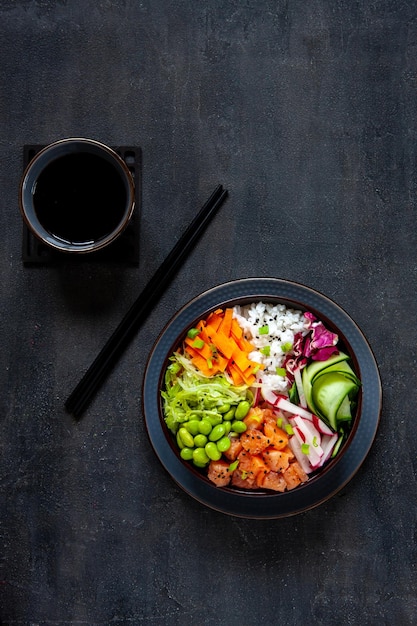 Colorful Asian trendy food sushi poke bowl with rice cucumber salmon carrot edamame beans and soy sauce Top view close up