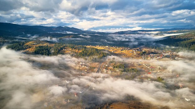 Colorful autumn morning over foggy mountain valley. Village covered by low clouds. Fall rural landscape. Misty cold November morning. Carpathians range, Ukraine, Europe.