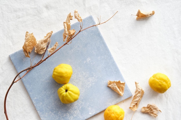 Colorful Autumn pattern with yellow quince fruits on blue ceramic tile Seasonal Fall still life arrangement on off white cotton textile tabletop Dry lime twigs with leaves