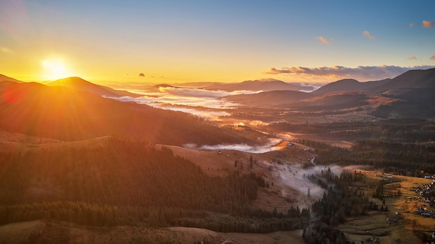 Colorful autumn sunrise over foggy woodland. Mountain forest covered by low clouds. Fall rural landscape. Village in misty valley. Cold November morning. Carpathians range, Ukraine, Europe.