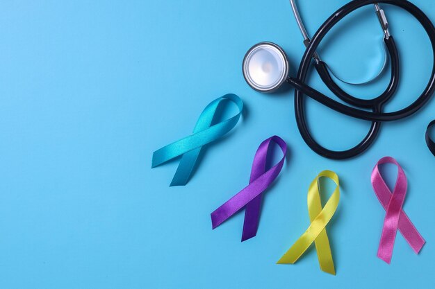 Colorful awareness ribbons teal purple yellow and pink color with stethoscope on blue background