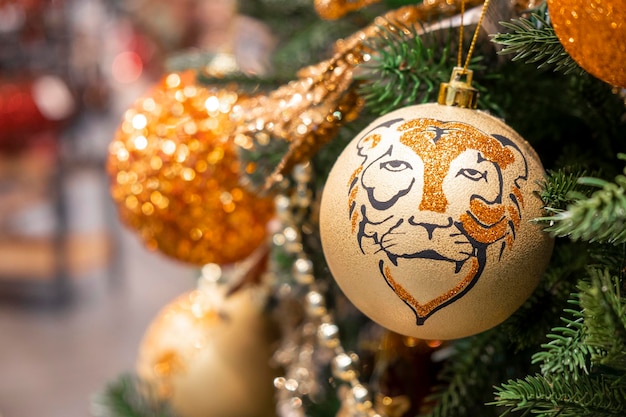 Colorful ball with tiger head ornament on christmas tree with\
bokeh lights on background. close-up christmas decorations. merry\
christmas and happy new year 2022 greeting card.