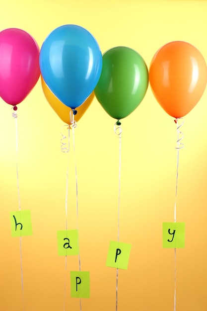 Foto i palloncini colorati mantengono la parola felice su sfondo giallo